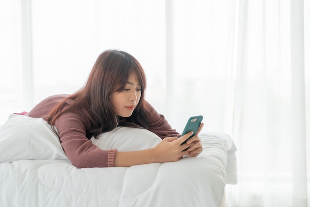 Aziatische vrouwen die smartphone op bed spelen