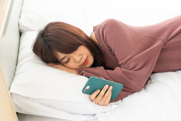 Aziatische vrouwen die smartphone op bed spelen
