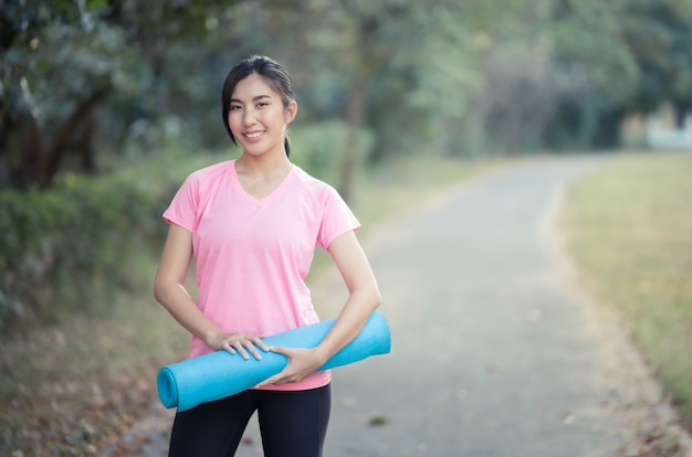 Aziatische vrouwen die yogamatten vasthouden, gaan yoga doen in het park om gezond te blijven en een goede conditie te hebben.