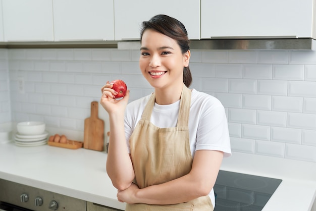 Aziatische vrouwen dragen een schort dat in de keuken thuis naar de camera kijkt, rode appel in de hand