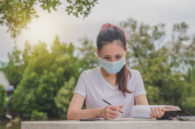 Aziatische vrouwen een het lezen van het leesboek van het gezichtsmasker openluchtzitting bij Universiteit