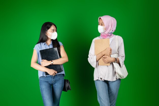 Aziatische vrouwen maskers die een laptop vasthouden terwijl ze naar elkaar kijken