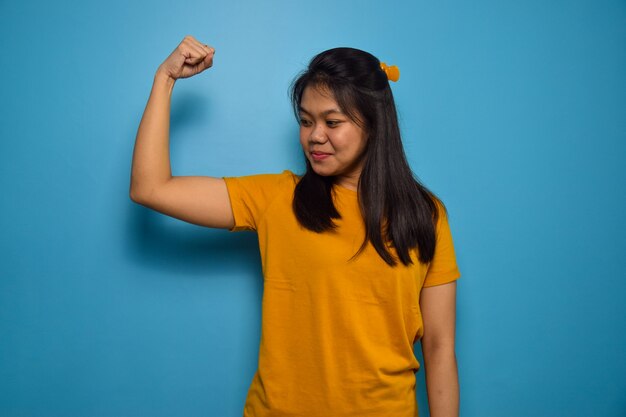 Aziatische vrouwen met een blauwe geïsoleerde achtergrond glimlachen en kijken naar de camera heft armen op en toont biceps