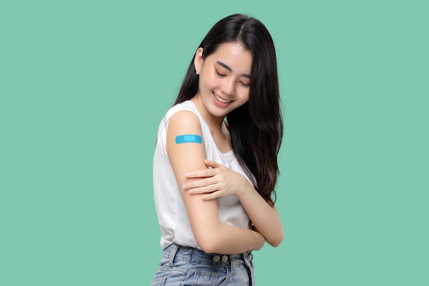 Aziatische vrouwen tonen verband op arm gelukkige aziatische vrouw voelt zich goed nadat ze vaccin heeft gekregen dat op groene achtergrond wordt geïsoleerd