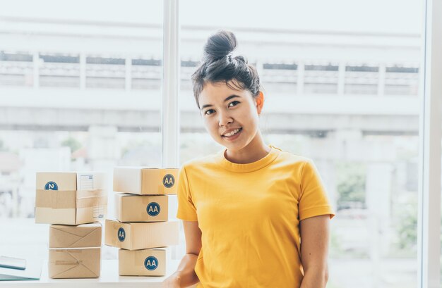Aziatische vrouwenbedrijfseigenaar die thuis met verpakkingsdoos aan werkplaats werken