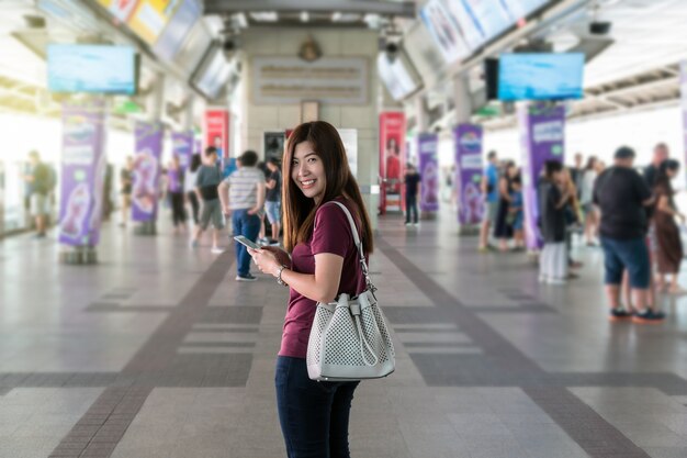 Aziatische vrouwenpassagier met toevallige reeks die de slimme mobiele telefoon gebruiken bij de uitwisseling tussen sta