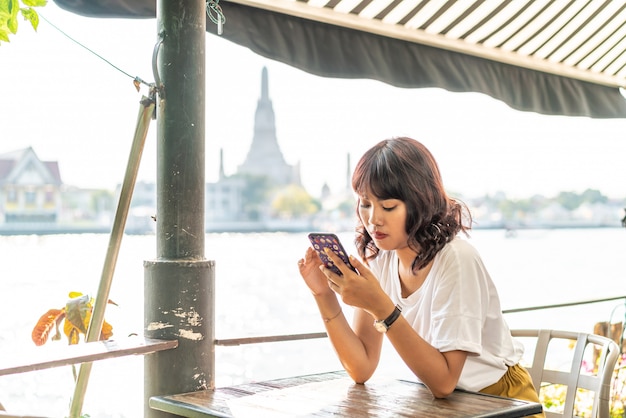 Aziatische vrouwenreiziger die haar telefoon in koffie met behulp van