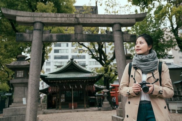 Aziatische vrouwentoerist die foto's in tenmangu-tempel nemen. jonge meisjestoerist die langs het actieve levensstijlconcept van osaka japan reist. mooie dame met camera met torii op de achtergrond buitenshuis.