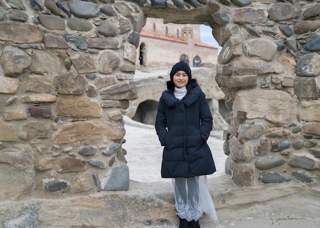 Aziatische vrouwentoerist die zich voor Rotsboog van de Ruïnes van de Grotstad Uplistsikhe bevindt die dichtbij de Archeologische Plaats van de Stad Gori in Georgië wordt gevestigd