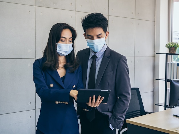 Aziatische zaken man en vrouw dragen pak en beschermende gezichtsmaskers met behulp van digitale tablet