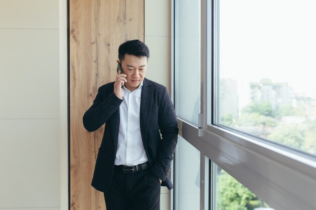 Aziatische zakenman die aan de telefoon in een modern kantoorcentrum praat, belt naar collega's