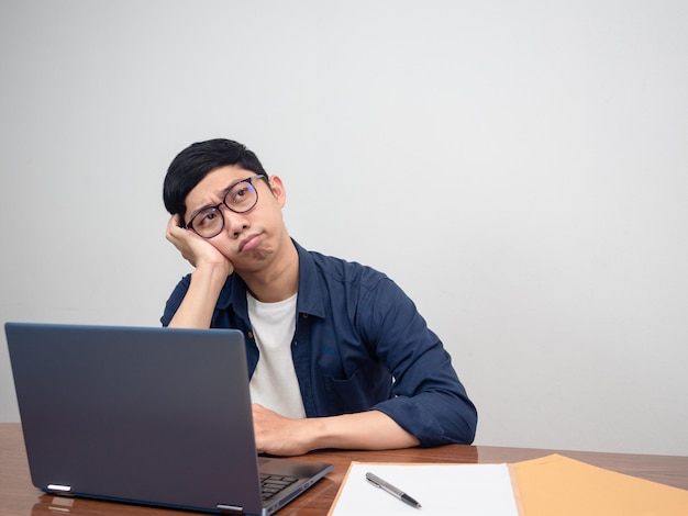 Aziatische zakenman die aan de werktafel zit, voelt zich beproefd en verveeld met werk