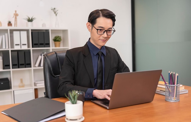 Aziatische zakenman die aan laptop in bureau werkt Succesvolle Aziatische zakenman die aan computer werkt