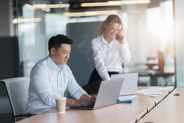 Aziatische zakenman die aan laptop werkt met collega op achtergrond