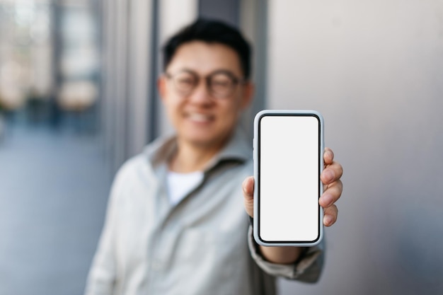 Aziatische zakenman die een leeg smartphonescherm toont bij camera die nieuwe mobiele app of websitemodel aanbeveelt