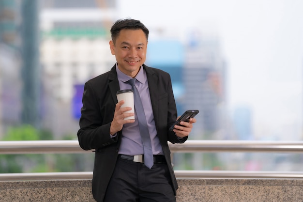 Aziatische Zakenman die en mobiele telefoon met bedrijfsbureaugebouwen bevinden zich in de stad
