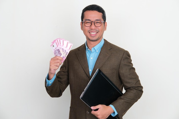 Aziatische zakenman die zelfverzekerd glimlacht terwijl hij een laptop en geld vasthoudt