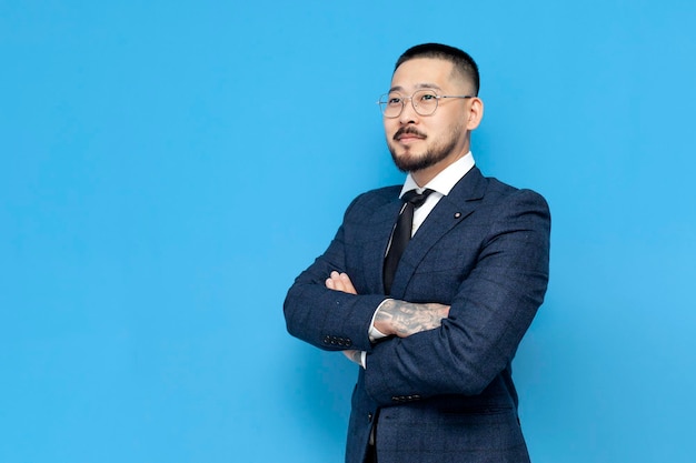 aziatische zakenman in pak en bril op blauwe achtergrond met zijn armen gekruist koreaanse ondernemer