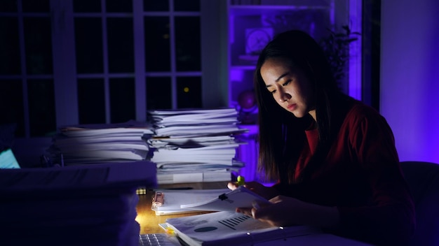 Aziatische zakenvrouw die in de late uurtjes hard werkt met veel documenten thuis. Druk en uitgeput van overwerk 's nachts.