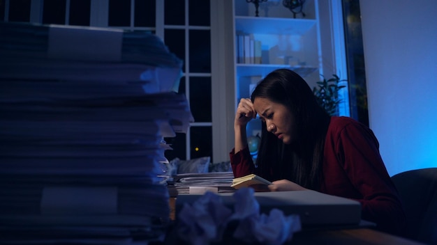 Aziatische zakenvrouw die in de late uurtjes hard werkt met veel documenten thuis. Druk en uitgeput van overwerk 's nachts.