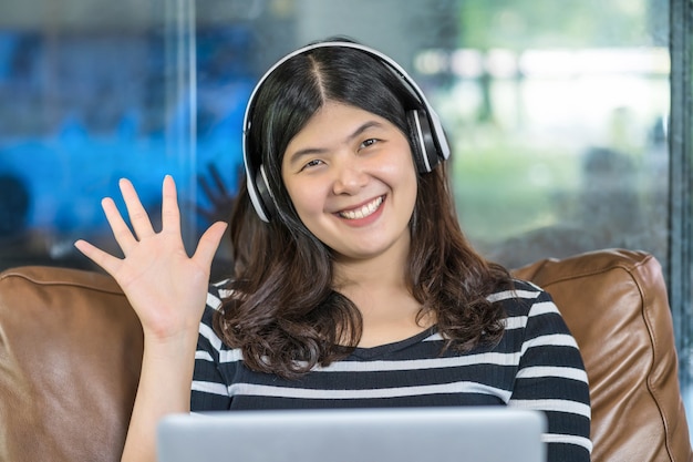 Aziatische zakenvrouw die met de hand zwaait om hallo te zeggen bij het maken van een videogesprek met een vriend