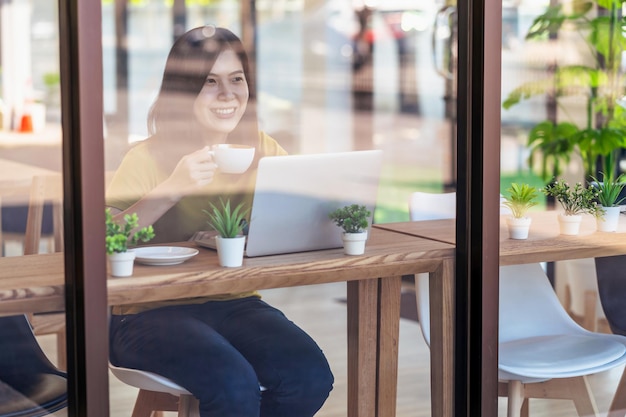 Aziatische zakenvrouw die thuis drinkt en werkt met een technologielaptop