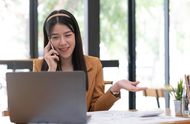 Aziatische zakenvrouw heeft de vreugde van praten op de telefoon laptop en tablet op het kantoor bureau