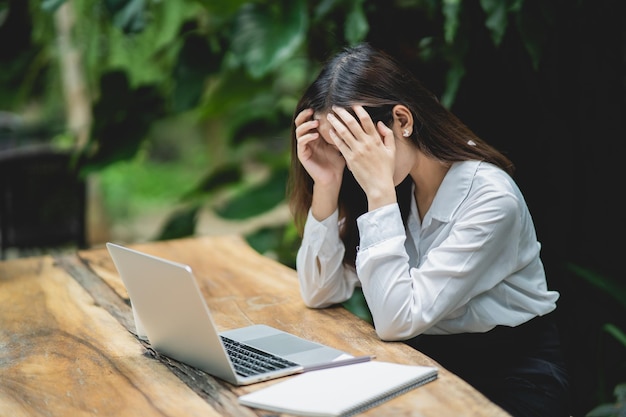 Aziatische zakenvrouw met stressvolle depressie trieste tijd werken op laptop op houten tafel Depressie man trieste serie die overal werkt