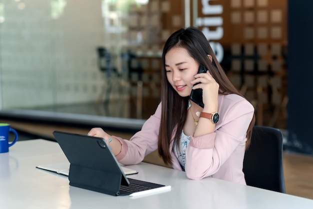 Aziatische zakenvrouw praten aan de telefoon met behulp van tablet op kantoor.