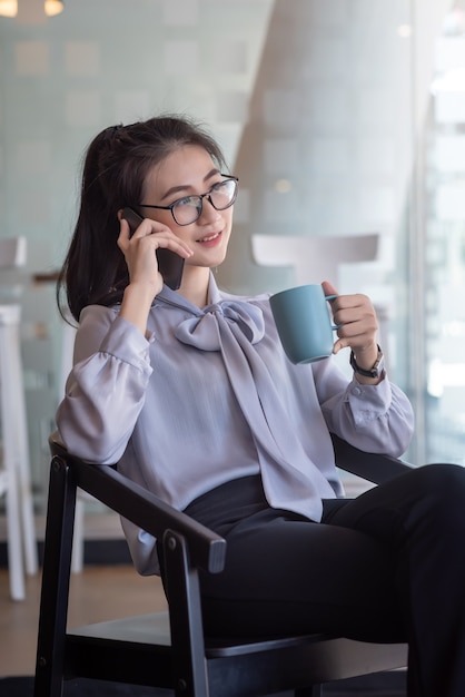 Aziatische zakenvrouw praten op de mobiele telefoon en koffie drinken op kantoor gelukkig