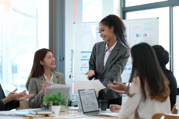 Aziatische zakenvrouwenleider in een ontmoeting met haar multi-etnische collega's op kantoor die verkoopgegevens of prognose voor een project presenteert