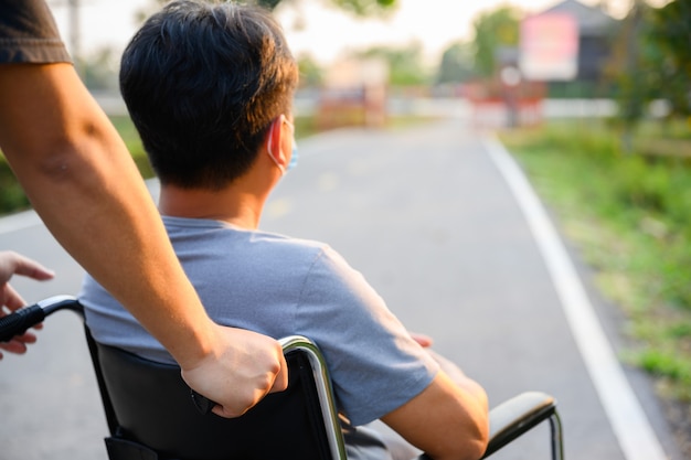 Aziatische zoon Lopen met gehandicapte vader in een rolstoel in het park Helpen gehandicapte vader die een rolstoel duwt