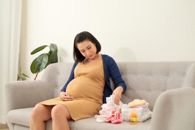 Aziatische zwangere vrouw aanstaande moeder bereidt kledingstukken voor de pasgeboren baby voor