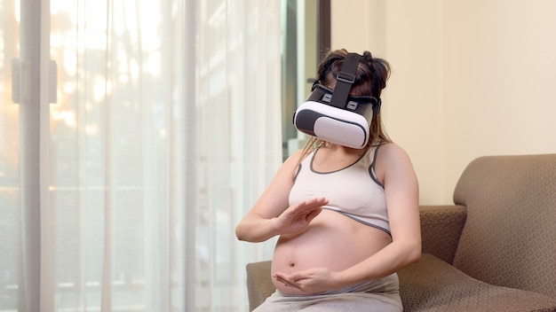 Aziatische zwangere vrouw die een virtual reality-headset draagt voor een ouderschapsproef. VR en technologie van zwangerschap.