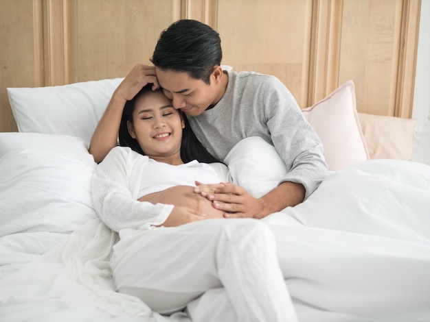 Aziatische zwangere vrouw en echtgenoot die op het bed leggen terwijl samen het doorbrengen van tijd.