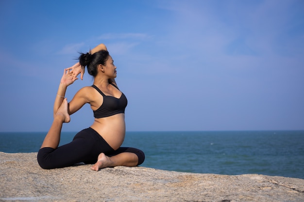 Aziatische zwangere vrouwenyoga op de de zomertijd van de strandzonsondergang