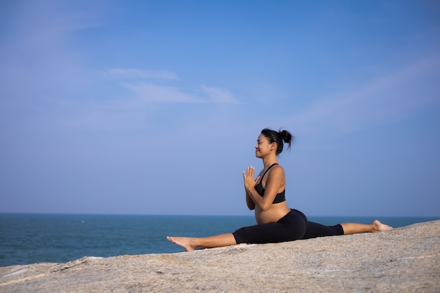 Aziatische zwangere vrouwenyoga op de de zomertijd van de strandzonsondergang