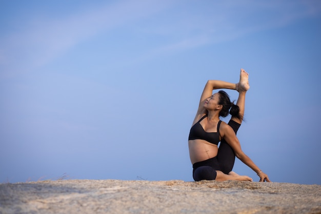 Aziatische zwangere vrouwenyoga op de de zomertijd van de strandzonsondergang