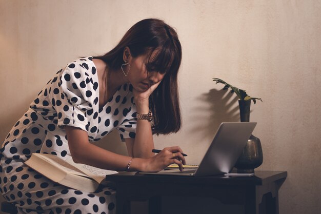 Foto azië vrouw leesboek en met behulp van laptop, notitie pad in vrije tijd met gelukkig