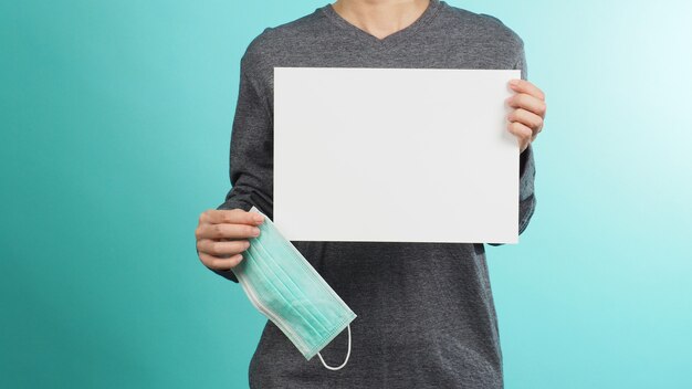 Azië Vrouwelijke handen houden gezichtsmasker of medisch masker en blanco A4-papier met grijs t-shirt op groene of Tiffany blauwe achtergrond.