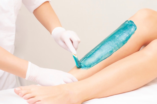 Azulene depilation. wax hair removal, shugaring. concept of smooth skin without hair. azulene of green color. the master puts azulene on the girls legs