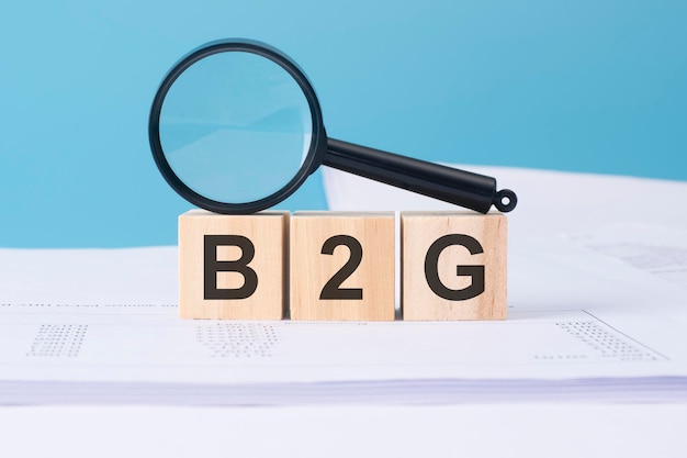 拡大鏡とビジネス ドキュメントで青色の背景に木製の立方体の B2G 単語