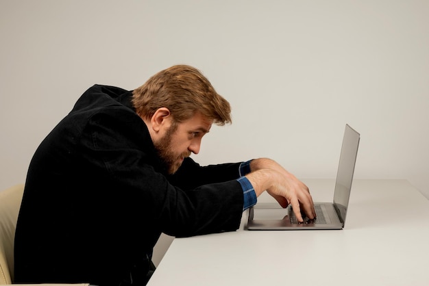 Baard emotionele man in slungelige positie zittend in kantoorruimte, werken met laptop