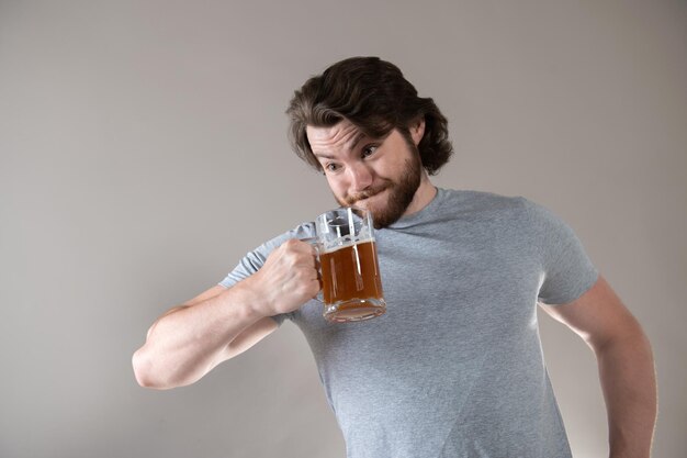 baarde man drinkt bier met een grote beker op een grijze achtergrond