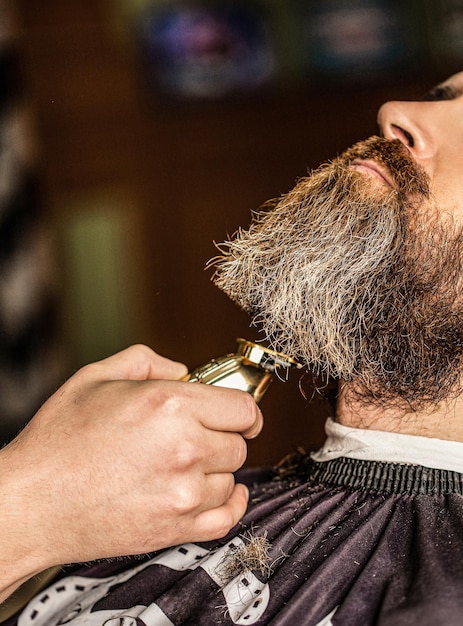 Baardige man in de kapperswinkel Barber werkt baardknipper Hipster klant wordt geknipt Handen van een kapper met een baardkniper close-up