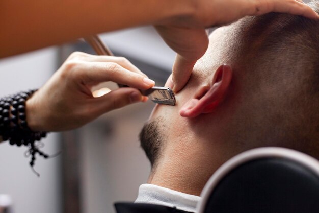 Baardkapsel in een kapperszaak een jonge man die zijn baard scheert met een scheermes close-up