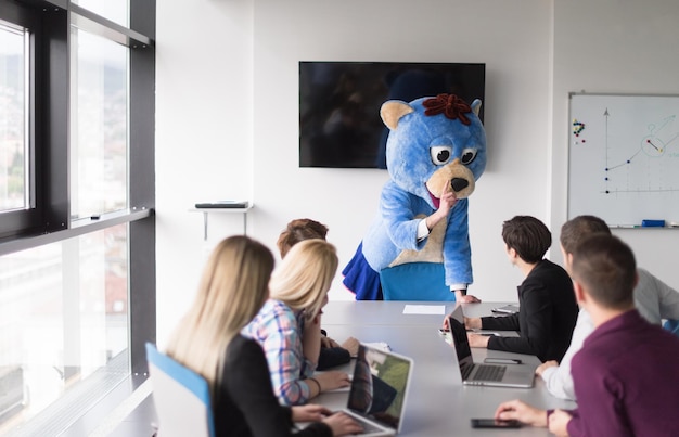 Baas verkleed als teddybeer die plezier heeft met zakenmensen in een modern hoofdkantoor