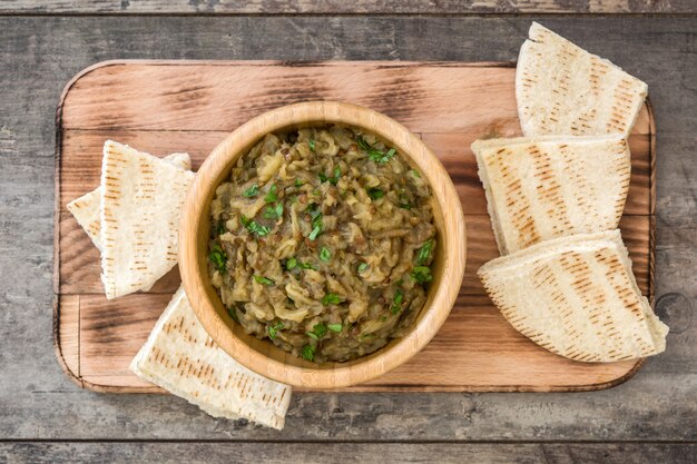 Photo baba ganoush in bowl and pita bread on wooden table, top view