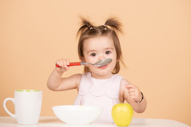 赤ちゃんのために健康的な食べ物を食べる赤ちゃんスタジオで隔離された面白い子供たちの顔でスプーンで健康的な食べ物を食べる子供