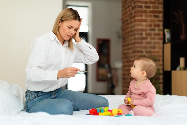 赤ちゃんと熱 ベッドに座っている病気の娘の世話をする体温計で kid39s の体温を測定するショックを受けた母親